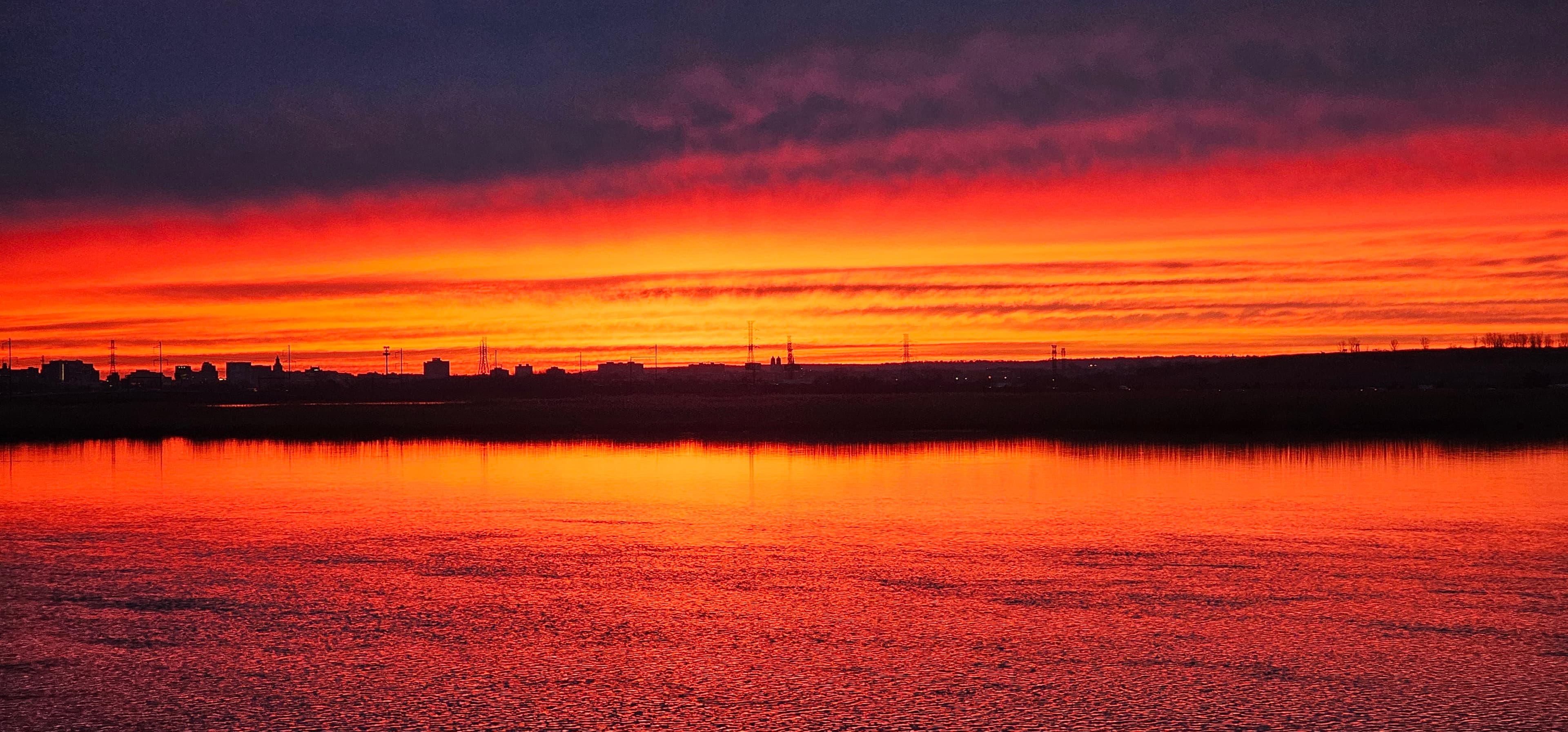 A fiery red and orange sunset mirrored across still water.